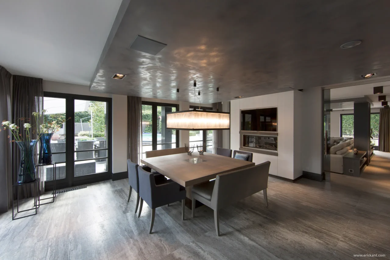 High-end eetkamer in project Family Country House met een vierkante houten eettafel, monumentale hanglamp, doorkijkhaard en natuurstenen vloer door ERIC KANT.