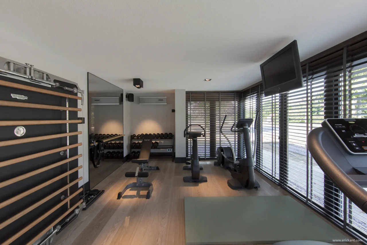 High-end privé sportschool in project Family Country House met houten vloer, professionele fitnessapparatuur, grote spiegelwand en zwarte shutters door ERIC KANT.