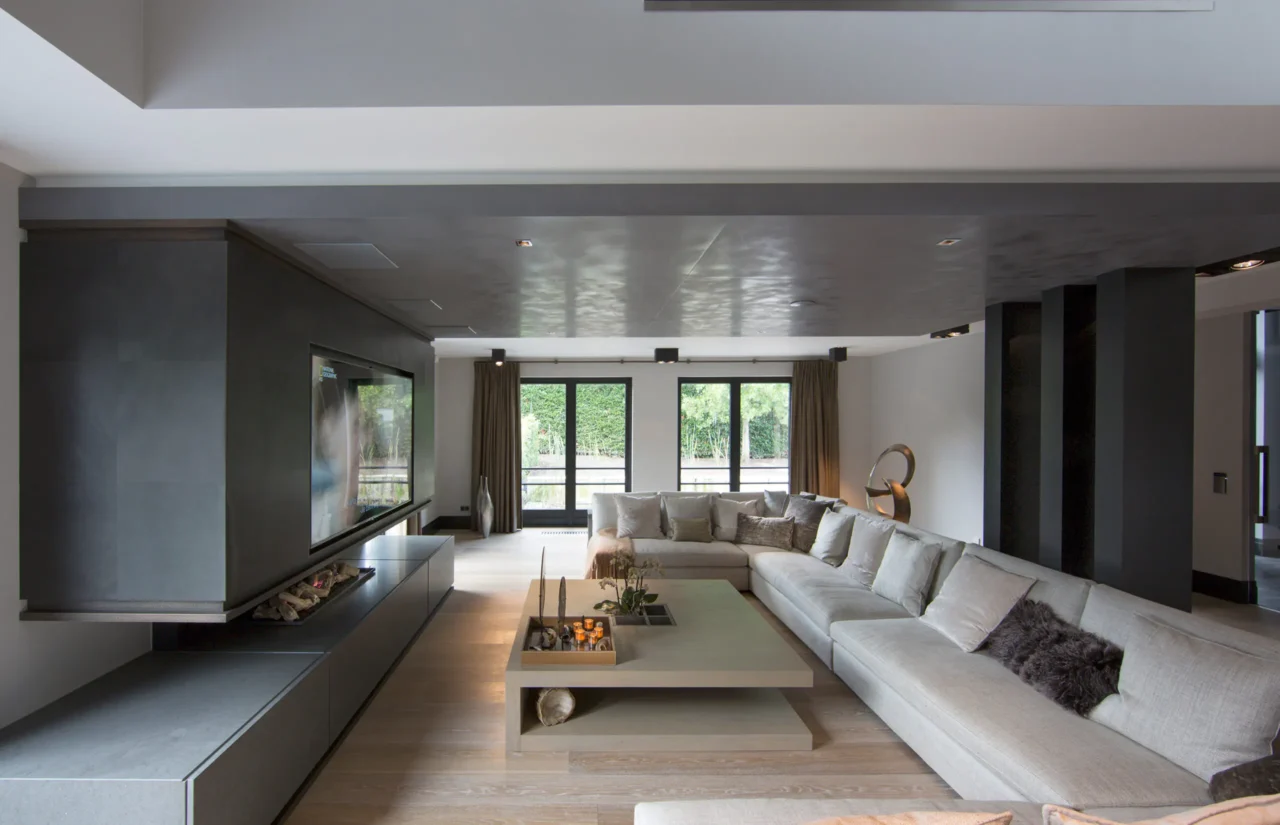 High-end woonkamer in project Family Country House met een monumentale zwevende haard, TV-meubel, grote hoekbank en een verlaagd betonlook plafond door ERIC KANT.