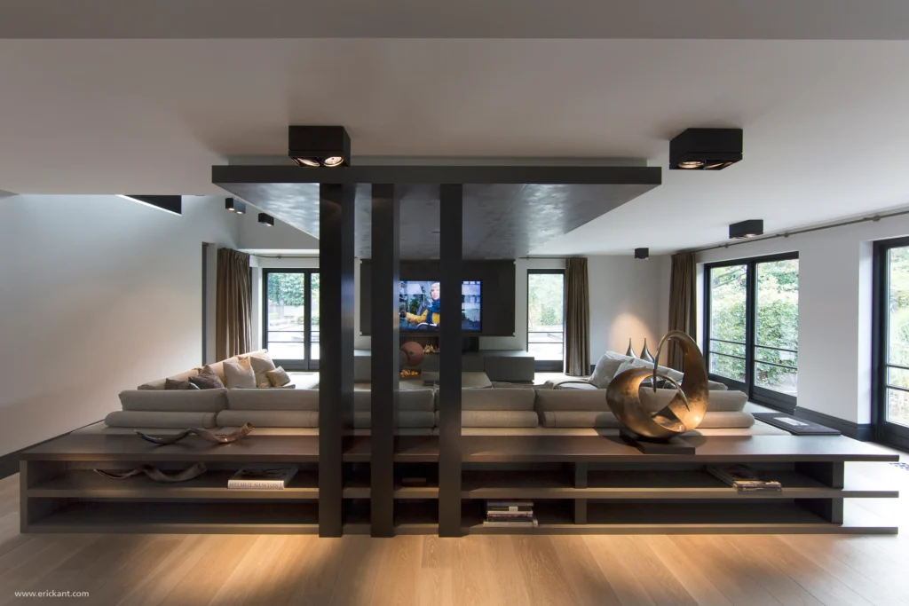 High-end woonkamer in project Family Country House met een symmetrisch houten maatwerk meubel achter de bank, zwarte verticale kolommen en een eikenhouten vloer door ERIC KANT.