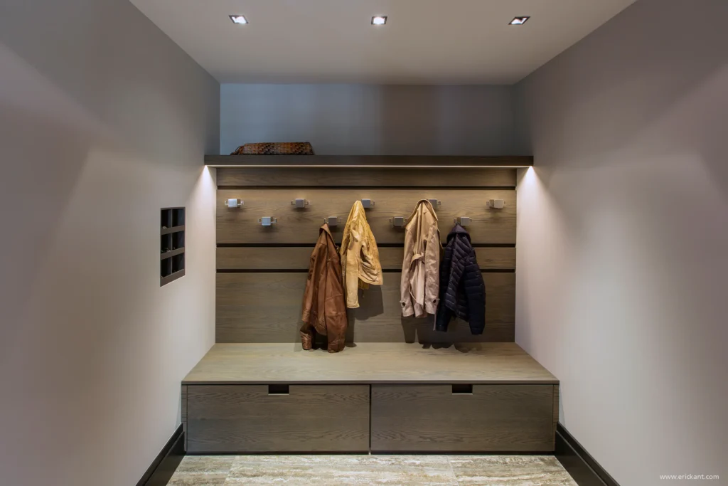 High-end garderobe in project Family Country House met eikenhouten wandpanelen, geïntegreerde haken, indirecte led-verlichting en een natuurstenen vloer door ERIC KANT.