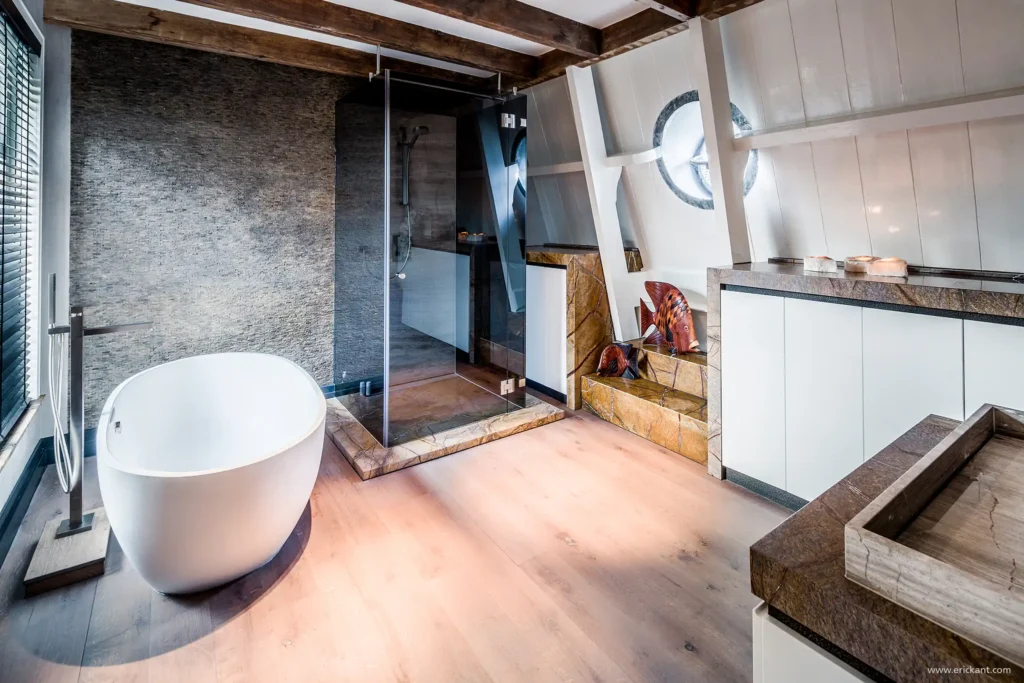 High-end badkamer in Riga met vrijstaand eivormig bad, glazen inloopdouche en natuurstenen accenten onder een schuin dak door ERIC KANT.