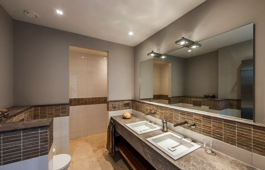 Luxe badkamer in het Luxury Bungalow project door ERIC KANT met een dubbele natuurstenen wastafel, mozaïek accentwanden, een grote spiegel met opbouwverlichting en een doorkijk naar de inloopdouche.