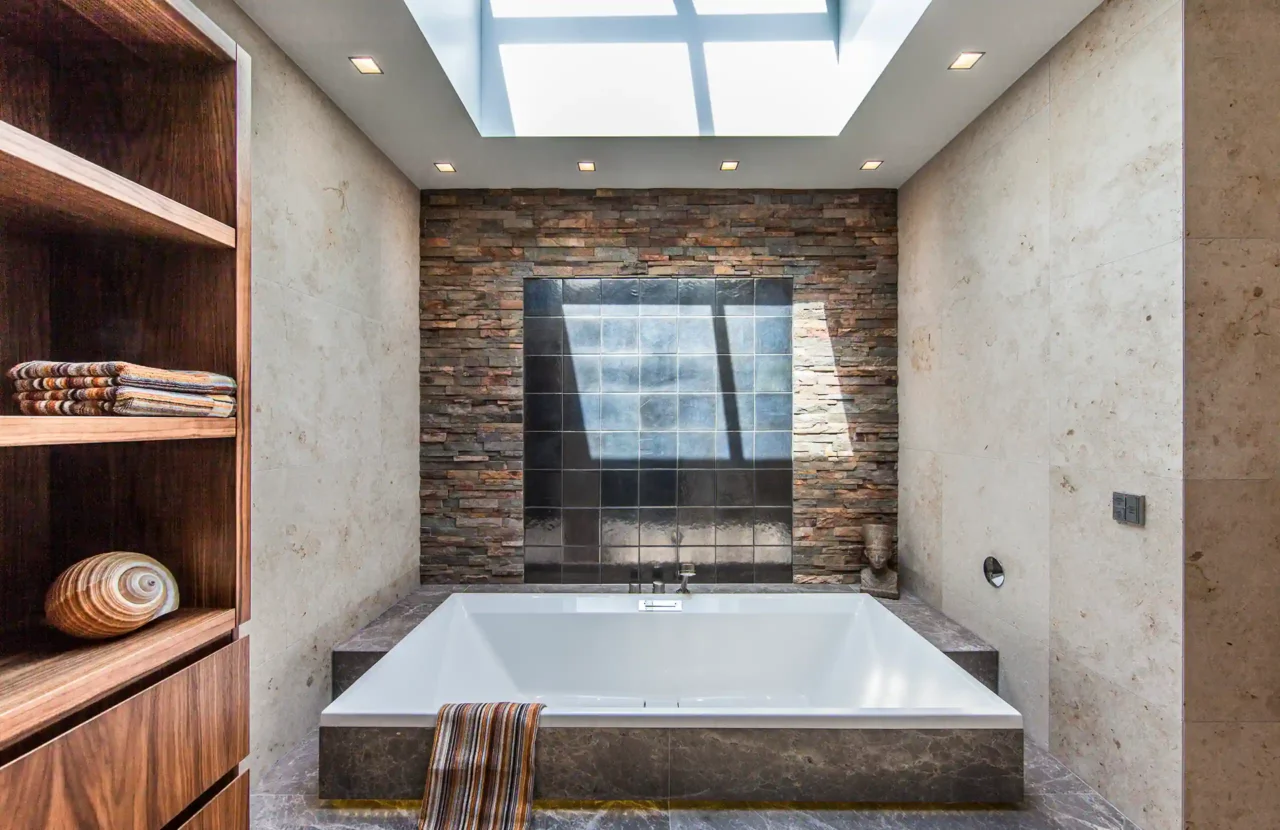 Luxe inloopdouche in het Luxury Bungalow project door ERIC KANT met mozaïek accenten, glazen wanden, een natuurstenen wastafelmeubel en zicht op de vrijstaande badkuip bij de rústieke natuurstenen wand.