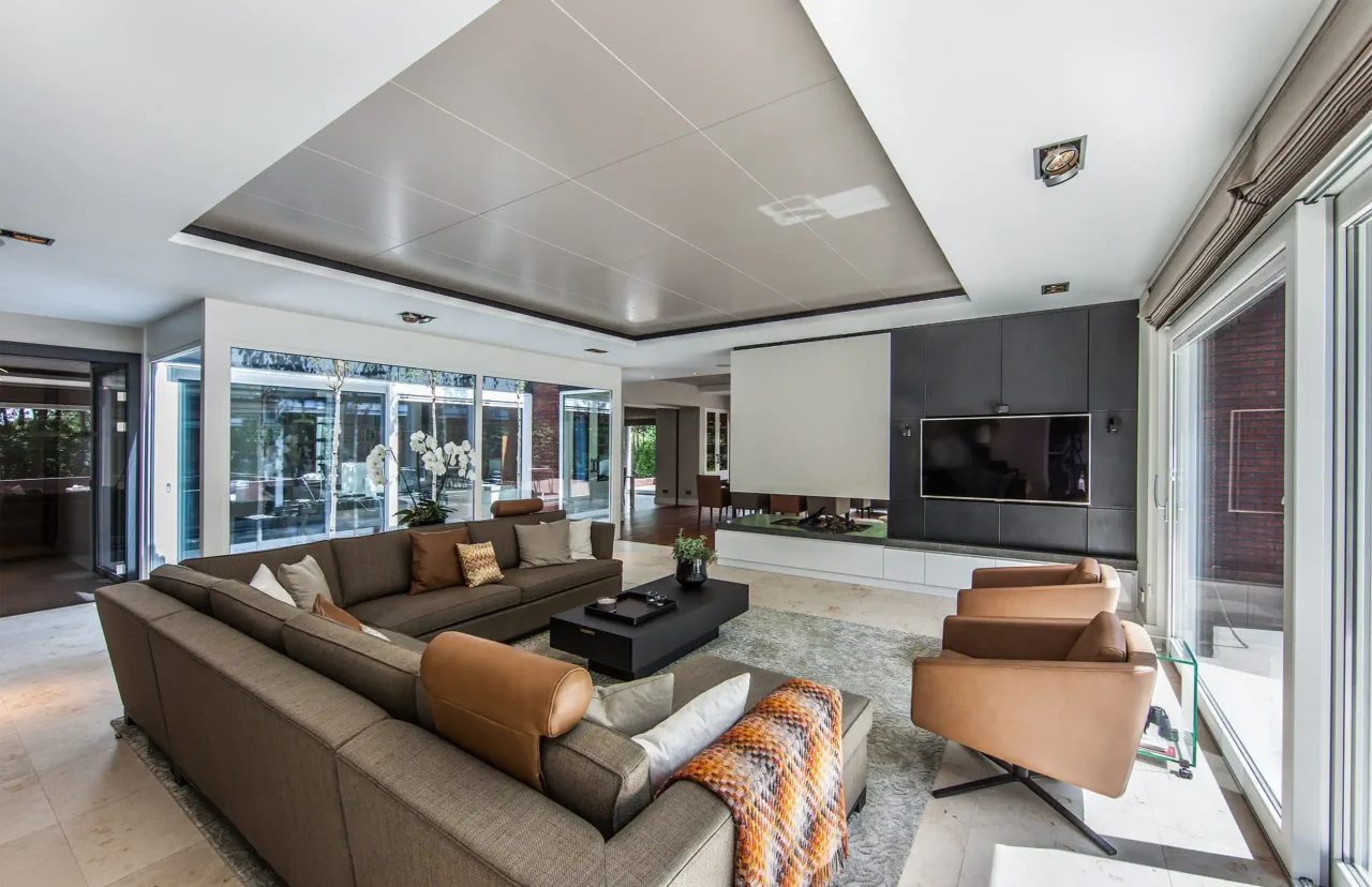 High-end living in het Luxury Bungalow project door ERIC KANT met een royale hoekbank, lederen fauteuils, een strakke TV-wand met open haard en grote glazen puien die uitkijken op de patio.