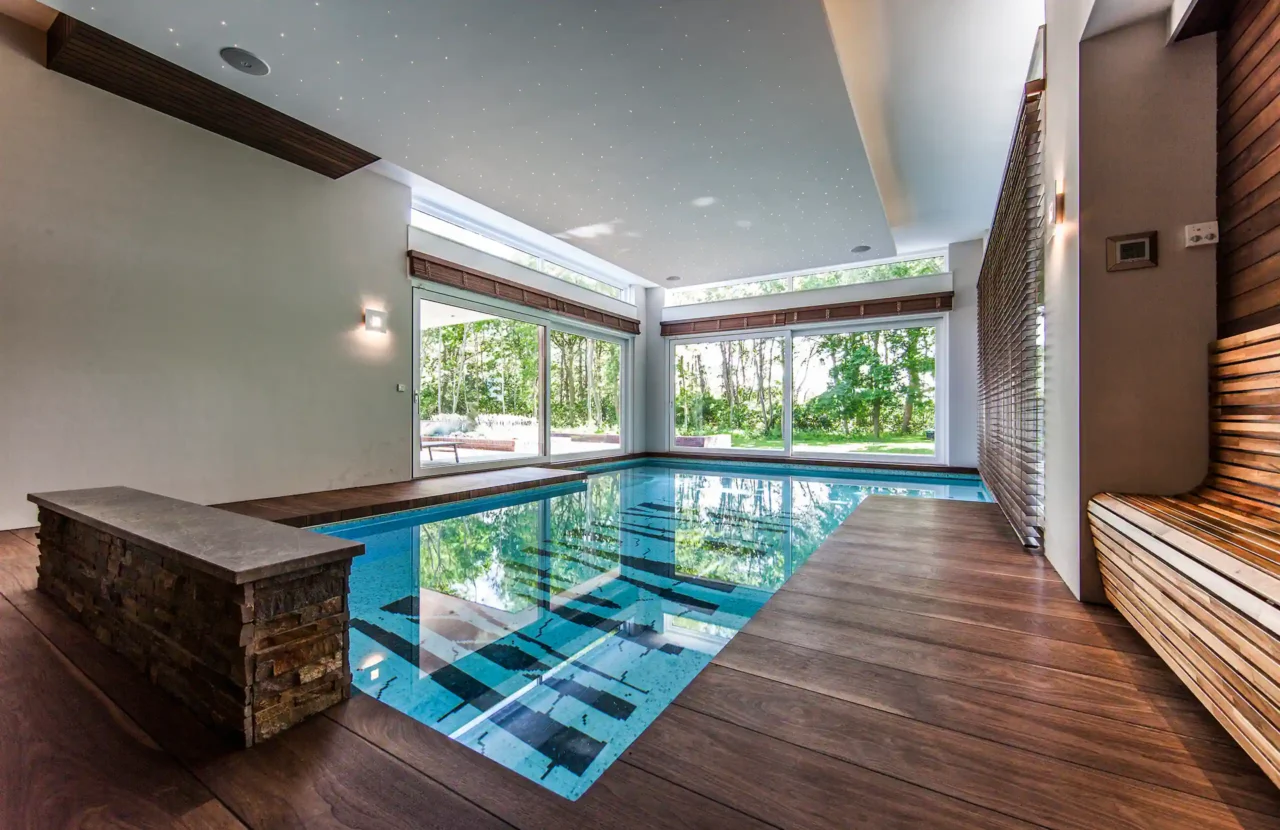Brede kijk op het binnenzwembad in het Luxury Bungalow project door ERIC KANT met houten vlonders, een stenen zitbank, sterrenhemel verlichting en panoramisch uitzicht op de tuin.