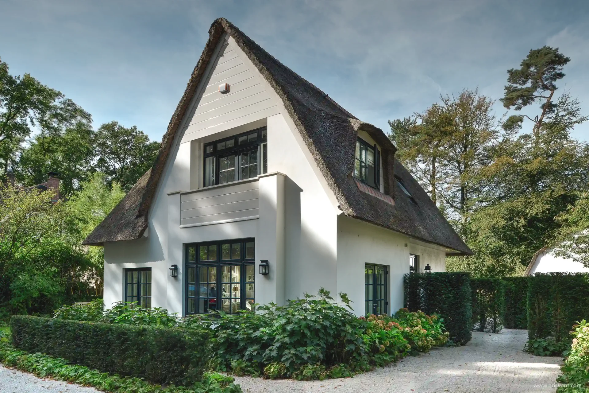Vooraanzicht van een klassieke villa in Laren door ERIC KANT met een rietgedekt dak en witte gevel, gecombineerd met een luxe houten overkapping inclusief glazen dak en eethoek.