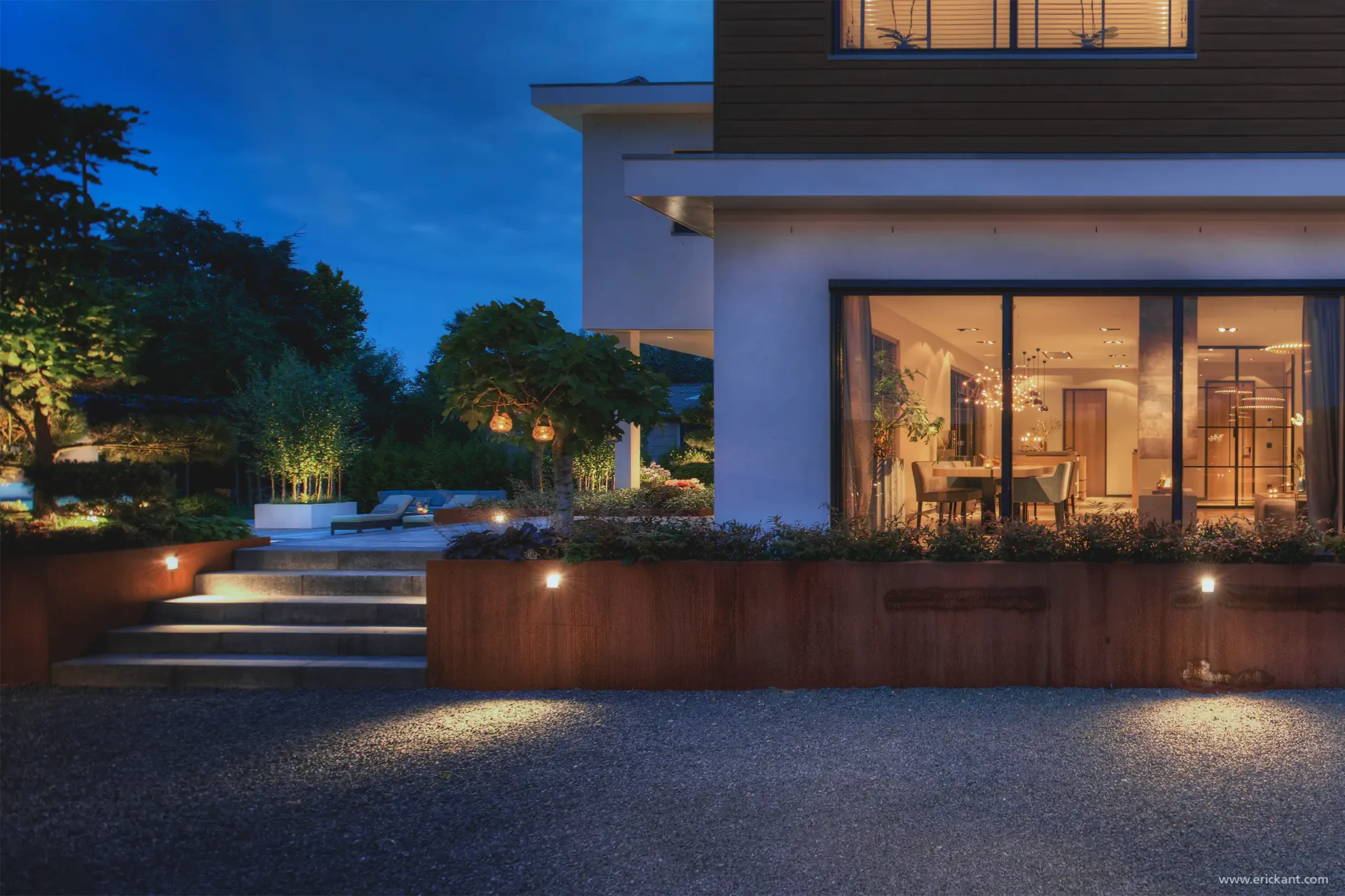 Exterieur van de Mediterranean Holland villa door ERIC KANT bij avond, met cortenstaal plantenbakken, sfeervolle tuinverlichting, een grindpad en grote raampartijen die een blik werpen op het warme interieur.