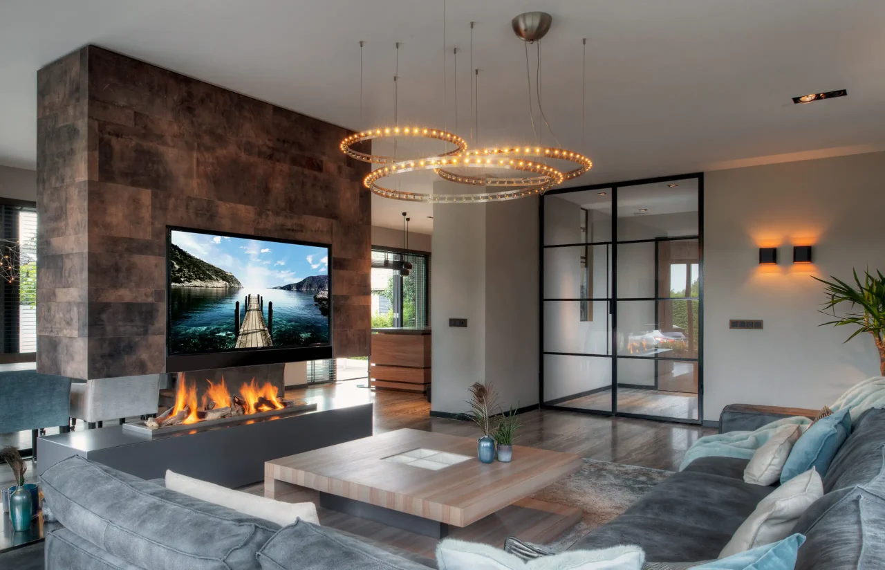 Interieur van de Mediterranean Holland villa door ERIC KANT met een gecombineerde haard- en tv-wand bekleed met bronzen panelen, een luxe zithoek, design ringverlichting en zwarte stalen deuren.