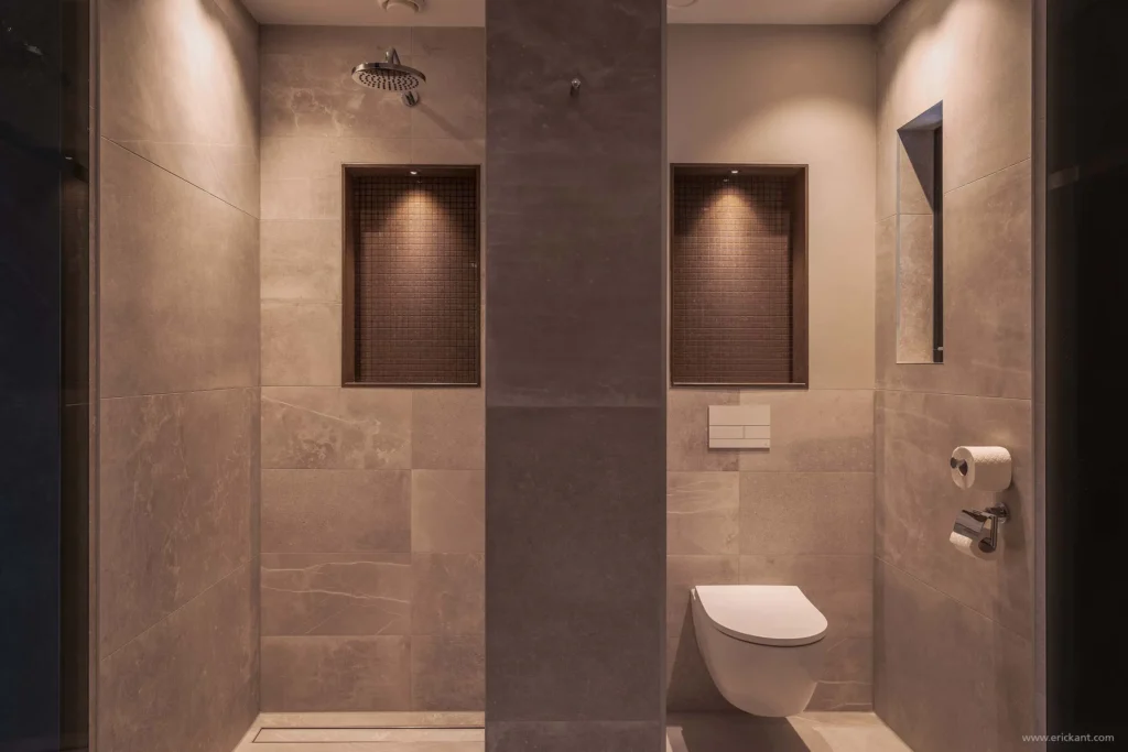 Interieur van een luxe badkamer door ERIC KANT met een dubbele wastafel van natuursteen, houten maatwerkkasten, een inloopdouche en een hangend toilet in een serene, zandkleurige setting.