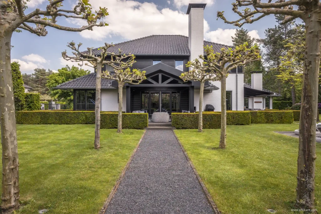 Achteraanzicht van de Renovation Villa door ERIC KANT met een contrastrijke witgekeerde gevel, zwarte houten accenten, een symmetrische tuin met grindpad en geknotte bomen.