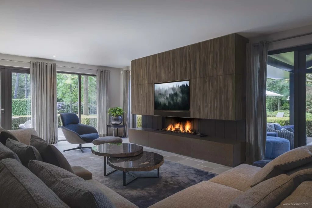 Interieur van de woonkamer in de Renovation Villa door ERIC KANT met een groot eikenhouten tv-meubel inclusief gashaard, een comfortabele zithoek en uitzicht op de tuin.