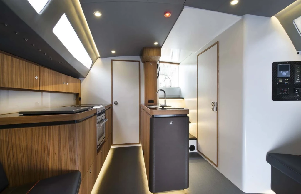 Modern interieur van een Agile Yacht ontworpen door Eric Kant, met een compacte houten keuken, rvs spoelbak, geïntegreerde oven en sfeervolle led-verlichting onder de kasten.