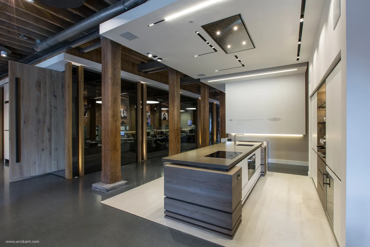 Een overzichtsfoto van de Bowers & Wilkins showroom door ERIC KANT met een modern kookeiland, robuuste houten kolommen, glazen kantoorwanden en een industriële gietvloer.