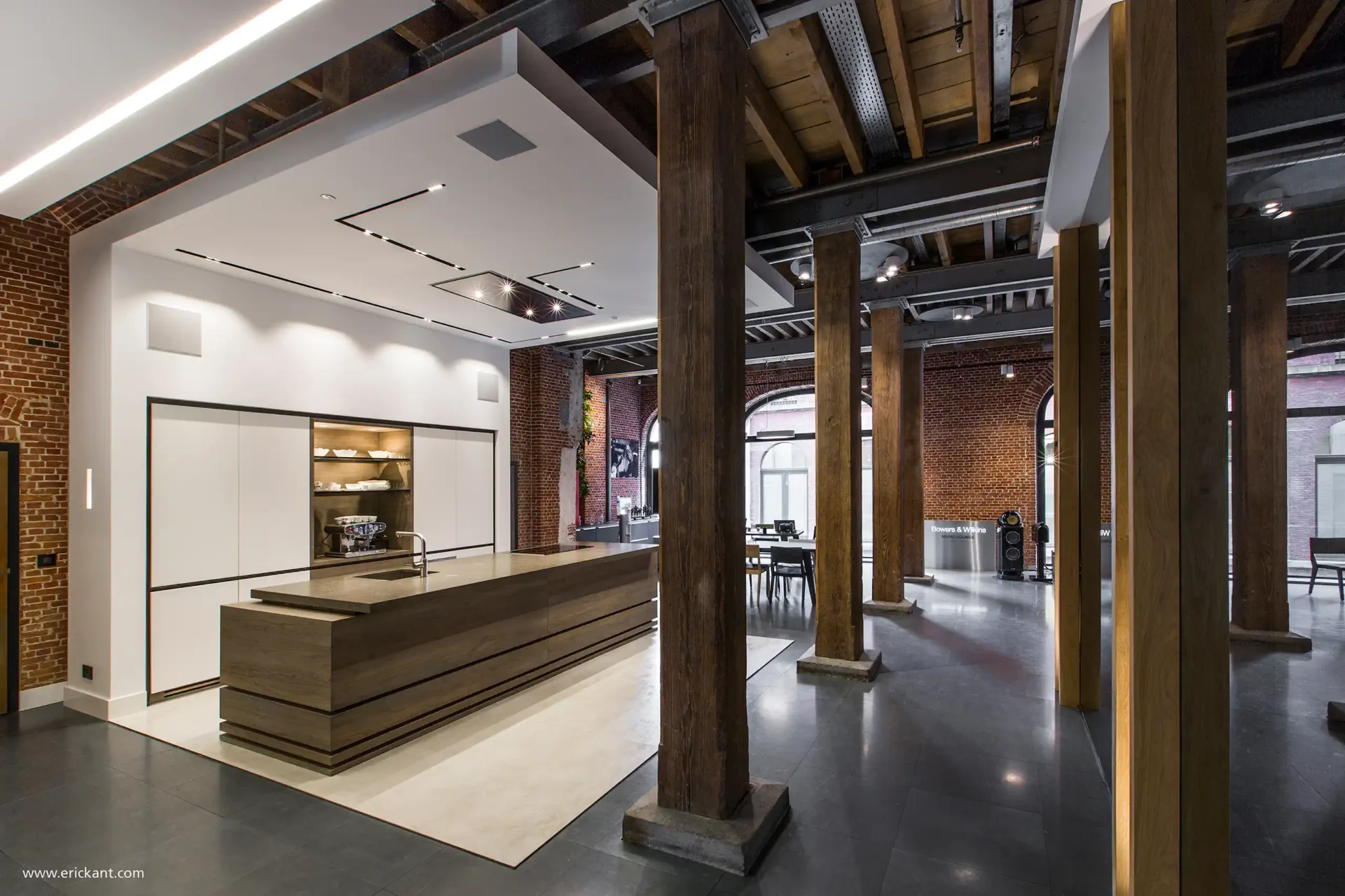 Groothoekopname van de Bowers & Wilkins showroom door ERIC KANT met een luxe designkeuken, monumentale houten kolommen, bakstenen muren en een doorkijk naar de Music Lounge.