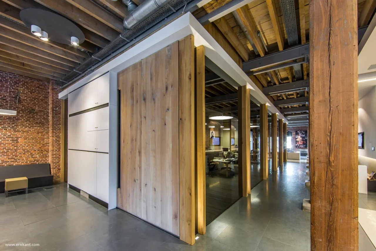 Een indrukwekkende kamerhoge eikenhouten pivotdeur ontworpen door ERIC KANT in het kantoor van Bowers & Wilkins, geflankeerd door een witte kastenwand en glazen kantoorunits in een industrieel pand.