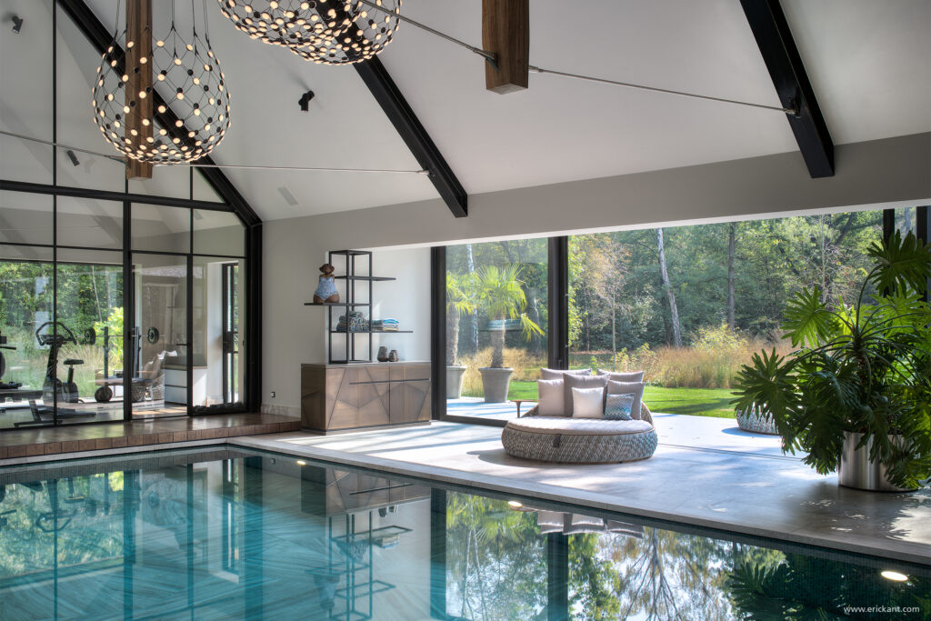 High-end pool-lounge van de Modern Manor met een turquoise betegeld binnenzwembad, houten dakspanten, grote glaswanden en een doorkijk naar de fitnessruimte door ERIC KANT.