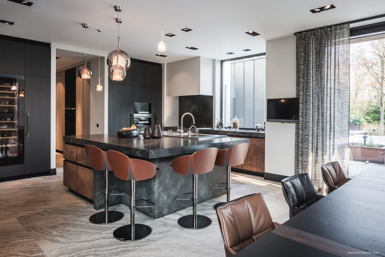 High-end keuken in de Modern Manor met een massief natuurstenen kookeiland, bronzen fronten, cognac lederen barkrukken, mondgeblazen hanglampen en een ingebouwde wijnklimaatkast door ERIC KANT.