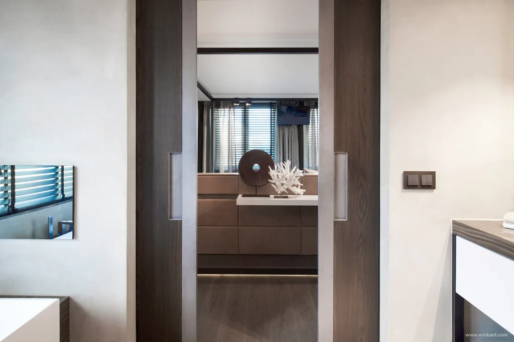 Zicht vanuit de badkamer van de Mansion on the Waterfront door ERIC KANT, door dubbele houten schuifdeuren met metalen afwerking naar de master bedroom met luxe decoratie en sfeerverlichting.