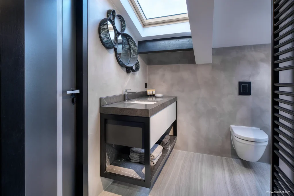 Interieur van een moderne kinderbadkamer in de Mansion on the Waterfront door ERIC KANT met een dakraam, betoncire wanden, een natuurstenen wastafelmeubel en decoratieve ronde spiegels.