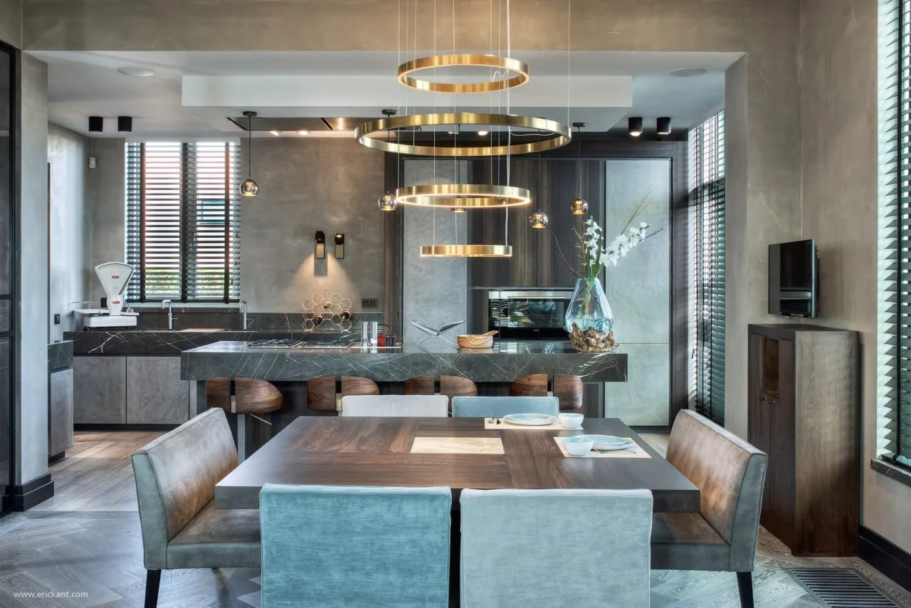 High-end woonkeuken en dining in de Mansion on the Waterfront door ERIC KANT met een massief marmeren kookeiland, een moderne kroonluchter met gouden ringen, betoncire wanden en maatwerk kasten.