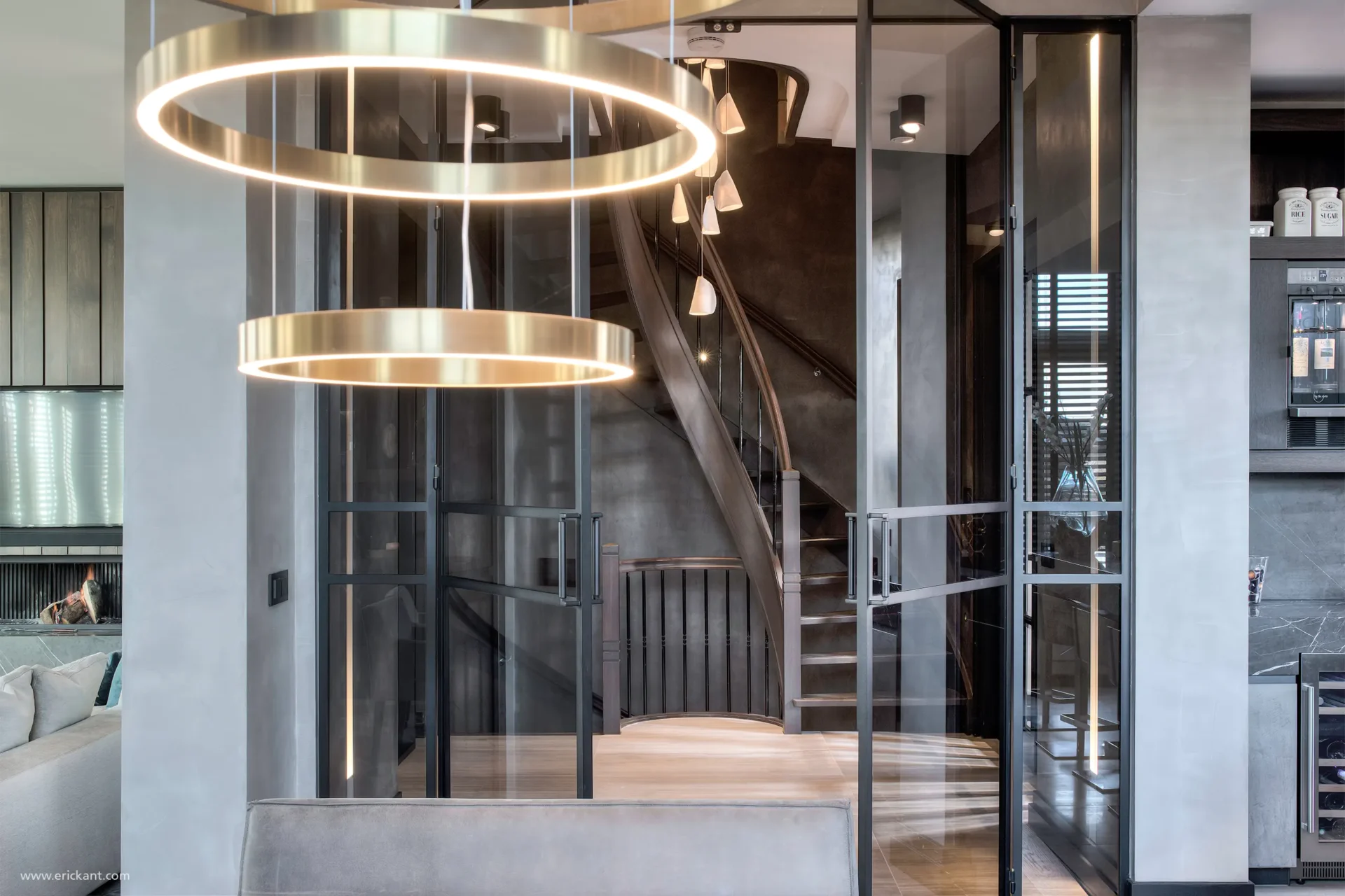 Interieur van de hal in de Mansion on the Waterfront door ERIC KANT met een imposante houten trap, stalen taatsdeuren, een moderne kroonluchter en zicht op de luxe living.Interieur van de hal in de Mansion on the Waterfront door ERIC KANT met een imposante houten trap, stalen taatsdeuren, een moderne kroonluchter en zicht op de luxe living.