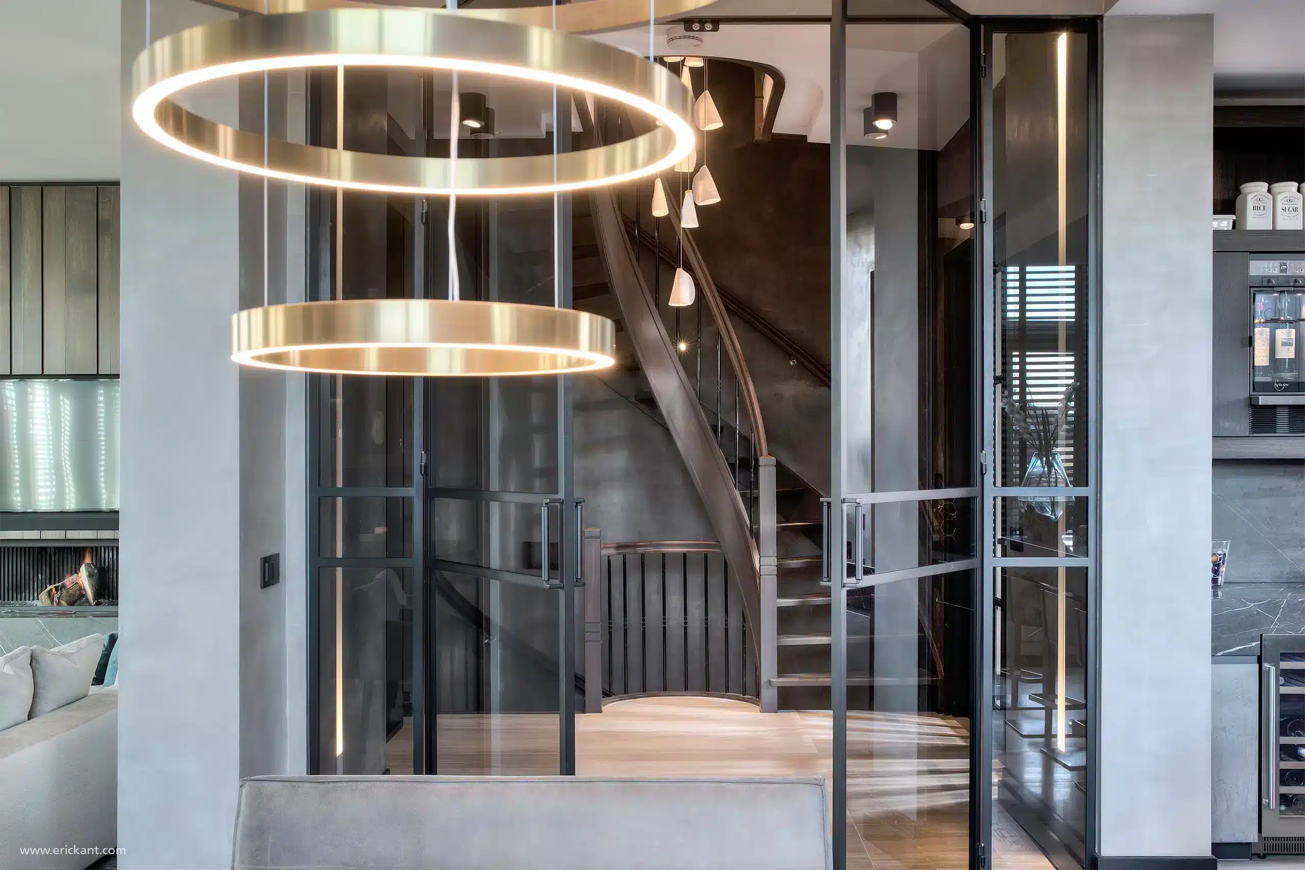 Interieur van de hal in de Mansion on the Waterfront door ERIC KANT met een imposante houten trap, stalen taatsdeuren, een moderne kroonluchter en zicht op de luxe living.Interieur van de hal in de Mansion on the Waterfront door ERIC KANT met een imposante houten trap, stalen taatsdeuren, een moderne kroonluchter en zicht op de luxe living.