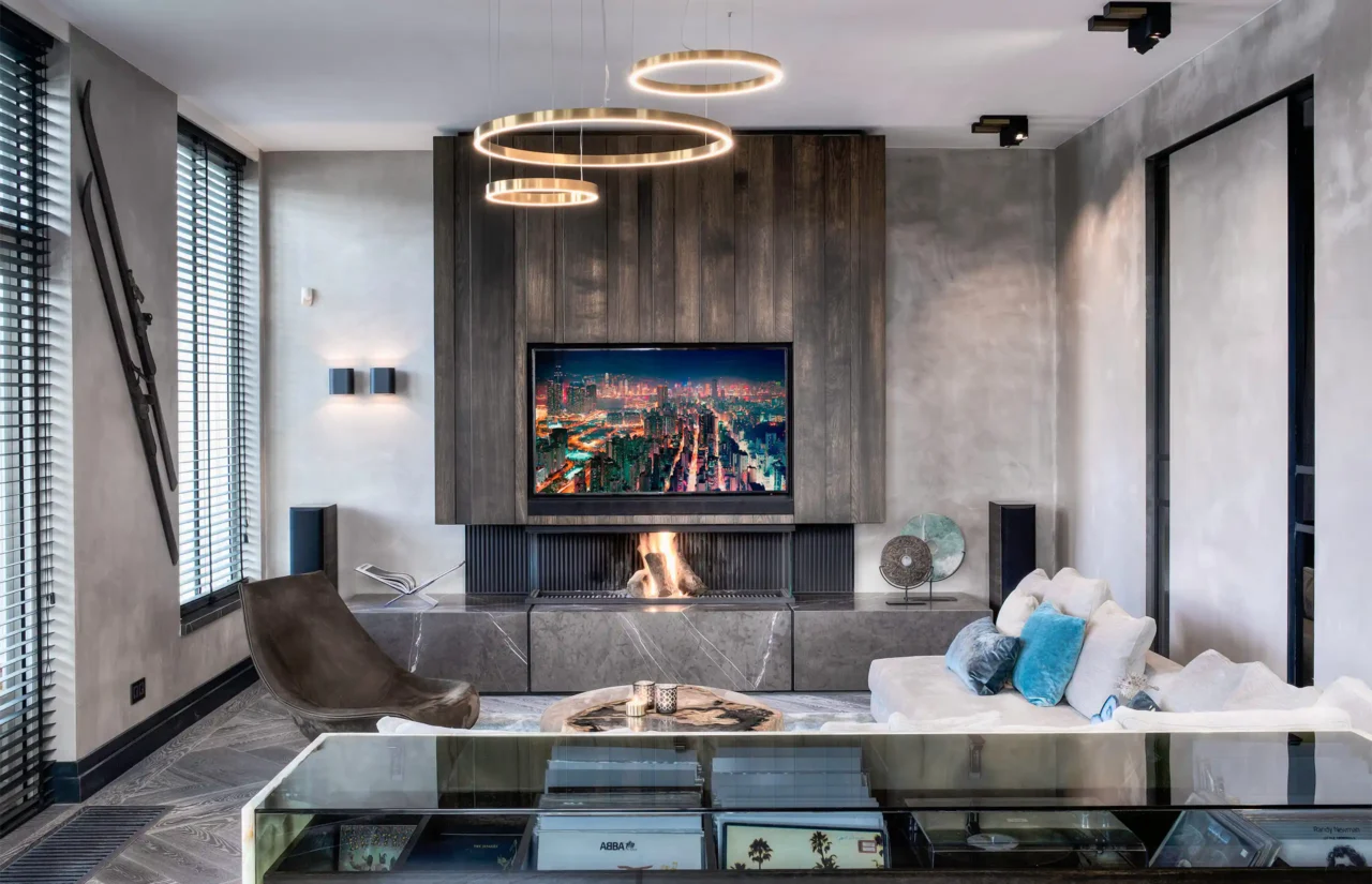 High-end living in de Mansion on the Waterfront door ERIC KANT met een maatwerk TV-wand in donker hout, een moderne gashaard op een marmeren plateau, betoncire wanden en gouden ringverlichting.