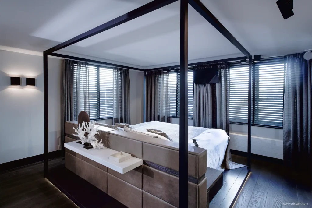 High-end master bedroom in de Mansion on the Waterfront door ERIC KANT met een zwart metalen hemelbed, een lederen maatwerk hoofdbord, luxe gordijnen en sfeervolle verlichting.
