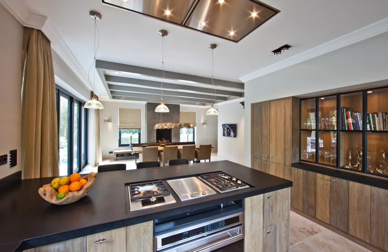 High-end keukeninterieur van project New Classic Villa met een professioneel kookeiland, eikenhouten kasten en zicht op de aangrenzende eetkamer met haard door ERIC KANT.
