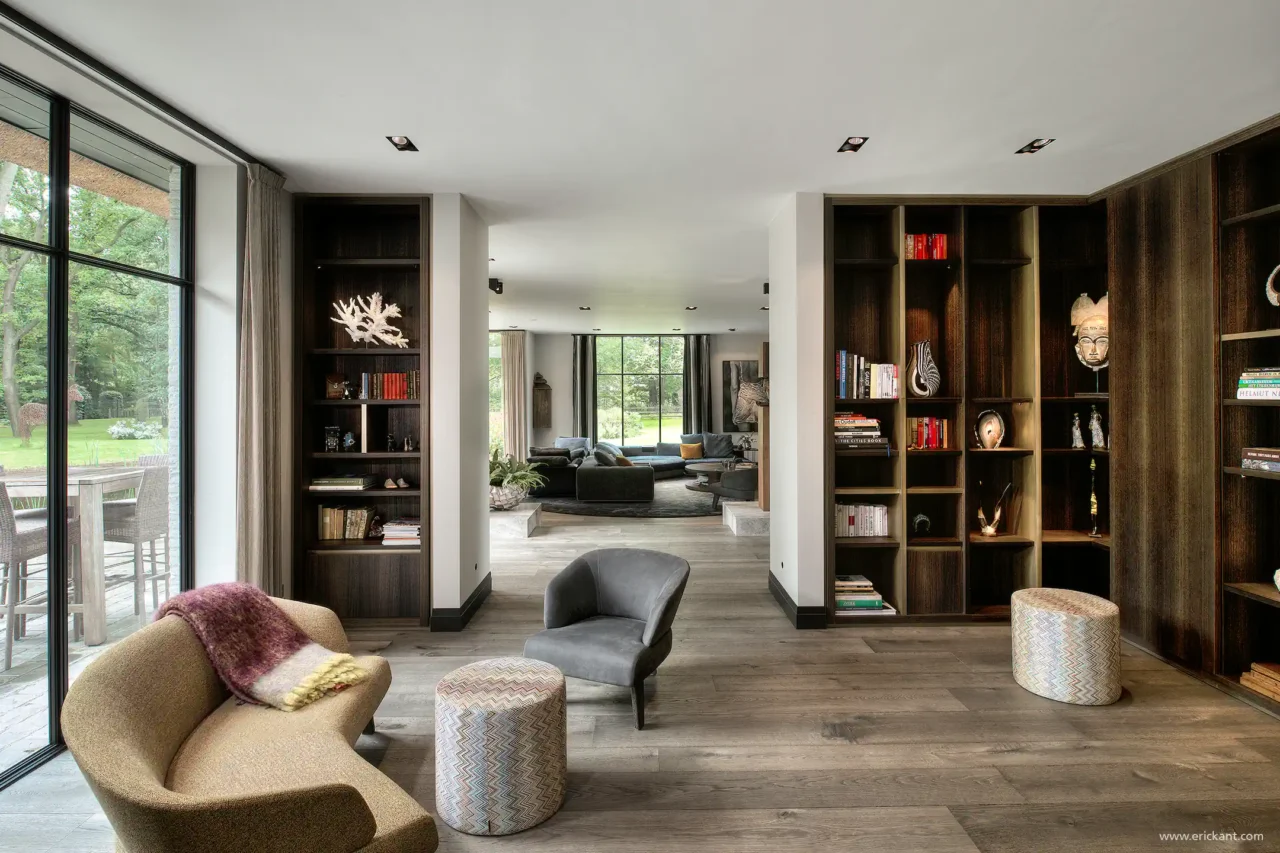 High-end interieur van de Modern Manor met kamerhoge houten maatwerkkasten, organische designmeubels, een eikenhouten vloer en zicht op de living door ERIC KANT.