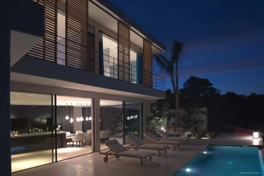 Luxe moderne villa in Ibiza bij nacht met verlicht zwembad, design buitenmeubilair en glazen gevel door ERIC KANT.