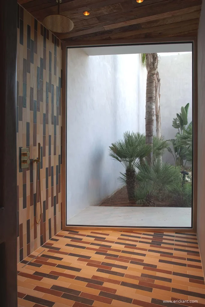 High-end inloopdouche met verticaal tegelpatroon, gouden regendouche en kamerhoog glas met uitzicht op een binnentuin in project Cali Moli Ibiza door ERIC KANT.