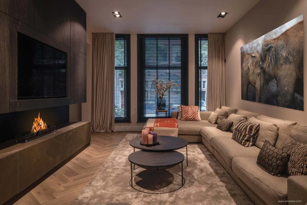 High-end woonkamerinterieur van project Modern Townhouse Amsterdam met een visgraatvloer, maatwerk kastenwand met tv en haard, en een grote hoekbank door ERIC KANT.