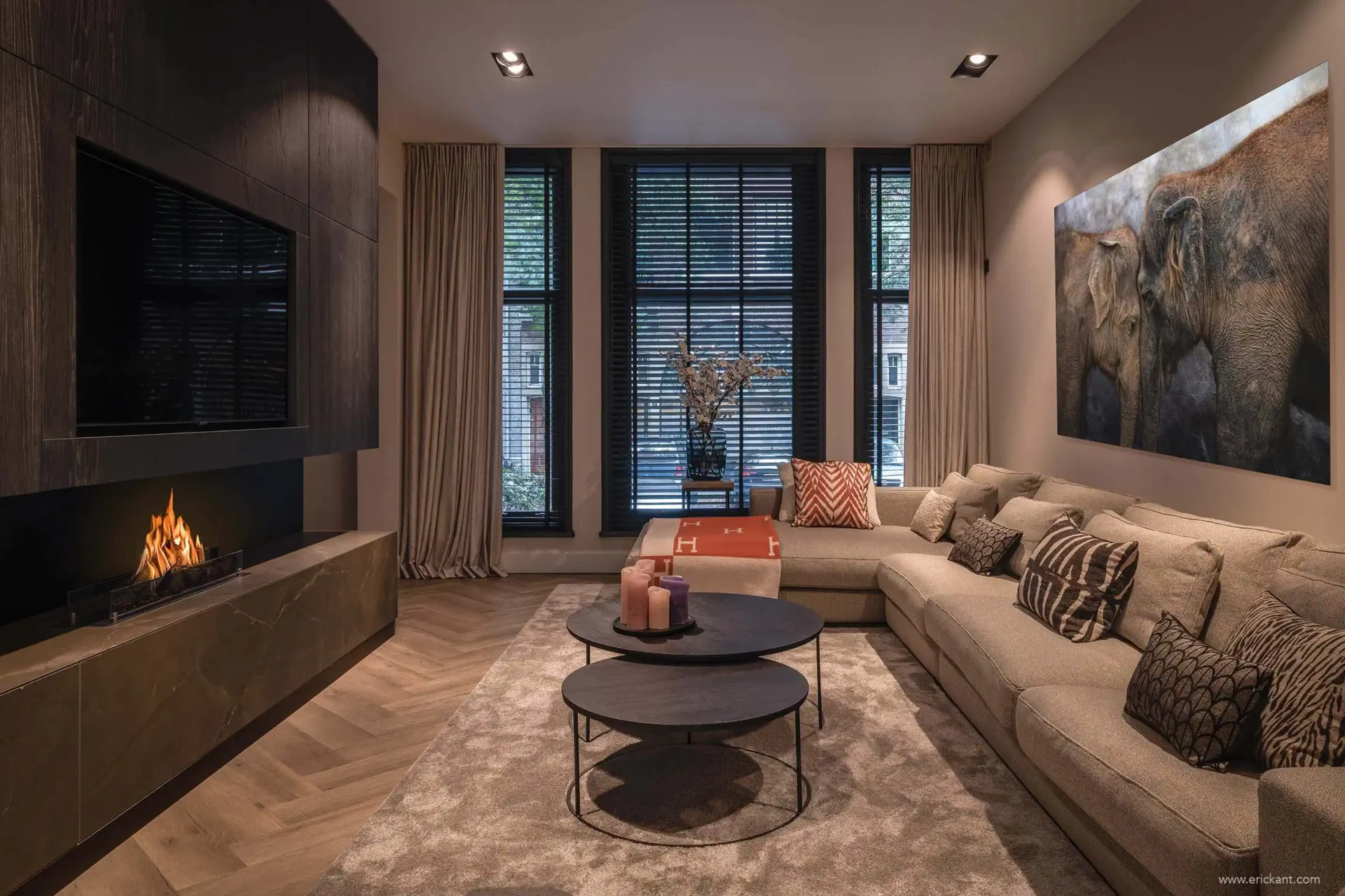 High-end woonkamerinterieur van project Modern Townhouse Amsterdam met een visgraatvloer, maatwerk kastenwand met tv en haard, en een grote hoekbank door ERIC KANT.