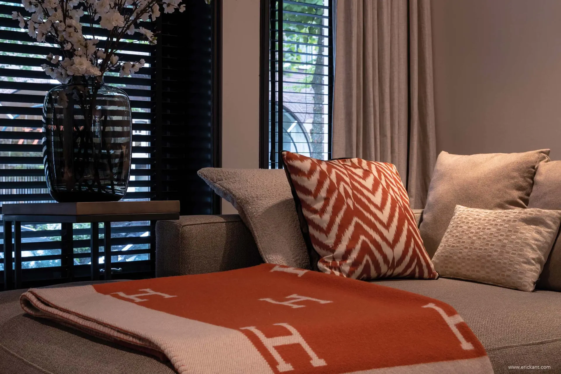 Detail van een luxe zithoek in de Modern Townhouse Amsterdam met een oranje Hermes-plaid, zigzag kussens en zwarte houten shutters op de achtergrond door ERIC KANT.