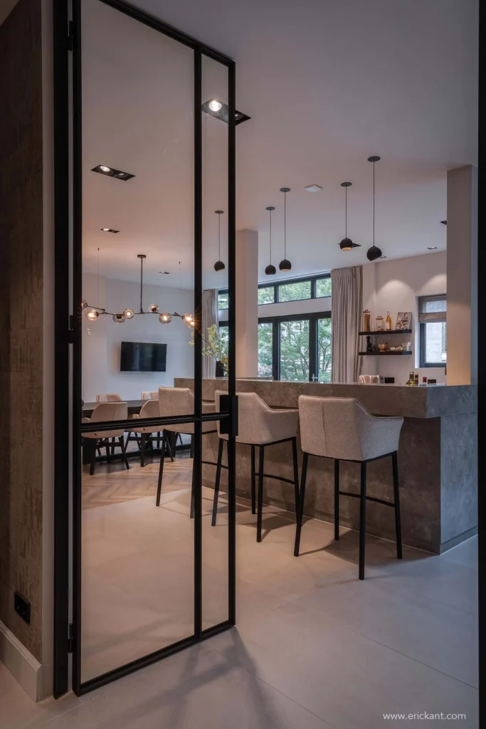 High-end interieur van de Modern Townhouse Amsterdam met zwarte stalen taatsdeuren, een marmeren keukenbar met luxe barkrukken en zicht op de eethoek door ERIC KANT.