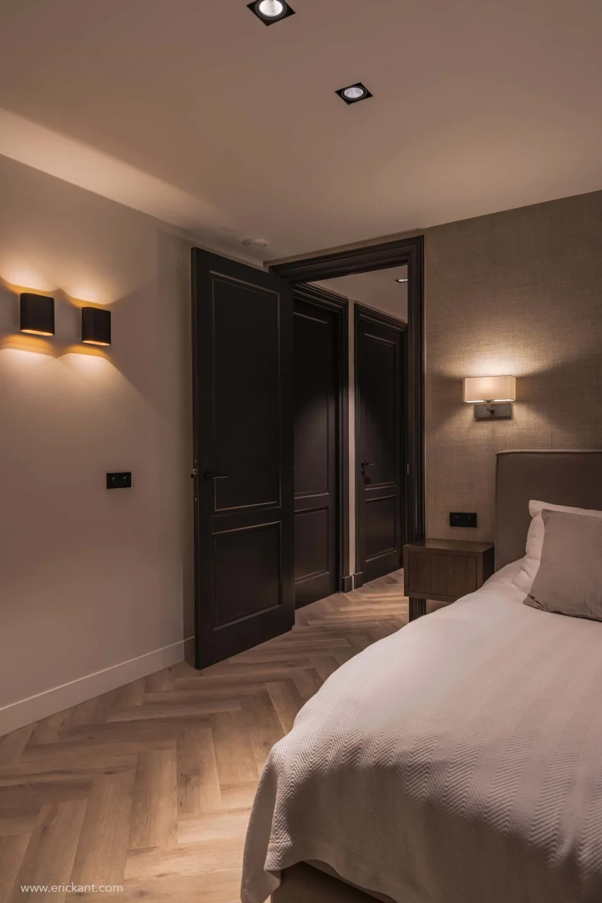 High-end slaapkamerinterieur van project Modern Townhouse Amsterdam met een visgraatvloer, zwarte paneeldeuren, wandverlichting en getextureerd behang door ERIC KANT.