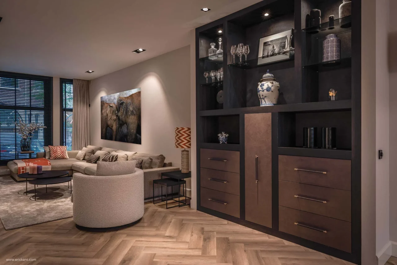 High-end interieur van de Modern Townhouse Amsterdam met een groot donker houten maatwerkkast, een zandkleurige hoekbank, visgraatvloer en sfeervolle verlichting door ERIC KANT.