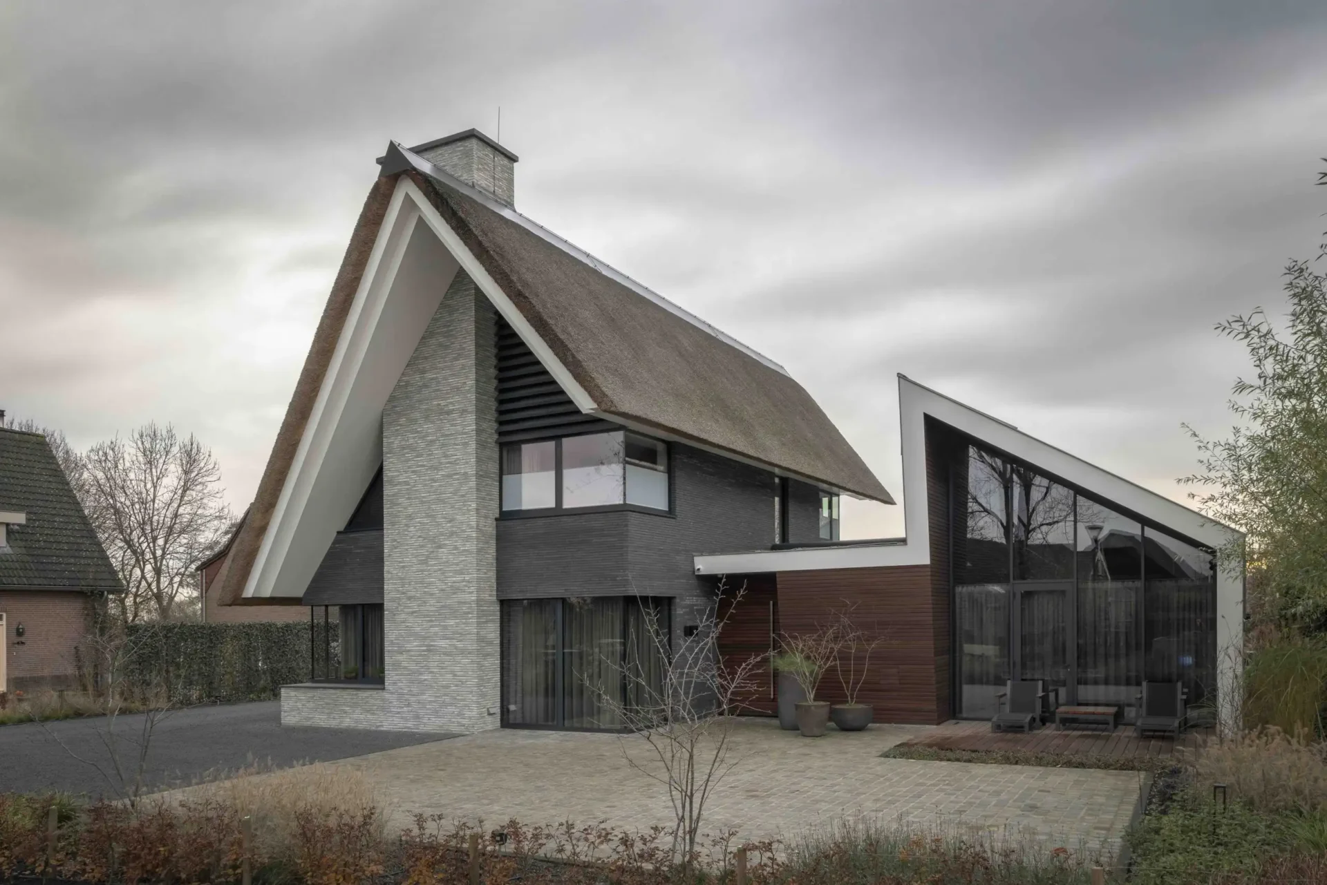 Exterieur van de Modern Classic Villa door ERIC KANT, met een rietgedekt dak, strakke witte dakranden, gevels van natuursteen en donkere baksteen, en grote glazen raampartijen.