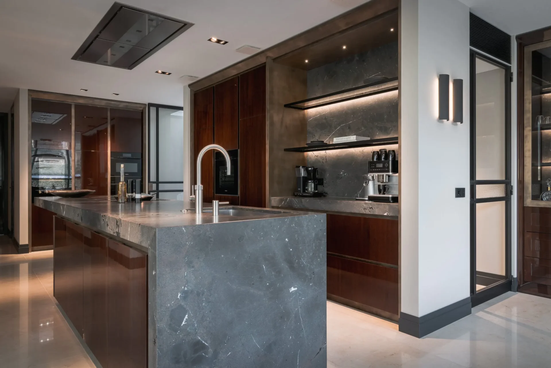 High-end keukeninterieur van de Modern Classic Villa met een massief natuurstenen kookeiland, hoogglans mahoniehouten kasten, een verlichte koffienis en een rvs designkraan door ERIC KANT.