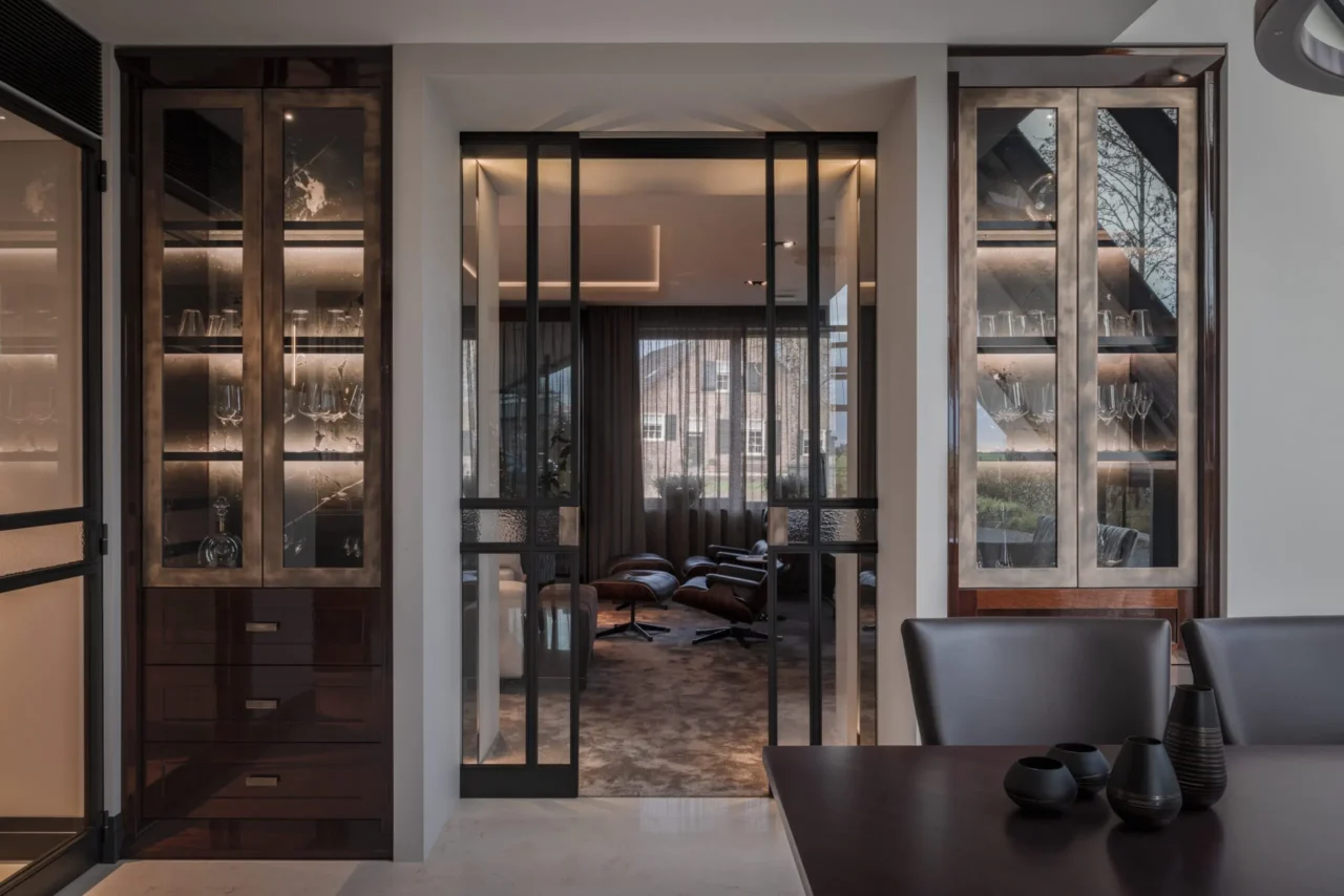 High-end interieur van de Modern Classic Villa met dubbele stalen schuifdeuren, geflankeerd door twee identieke maatwerkkasten in hoogglans mahonie en brons door ERIC KANT.