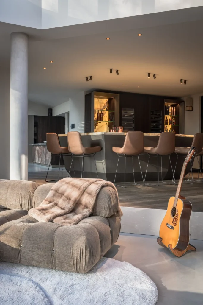 Interieur van de Metropolitan Luxury villa door ERIC KANT met zicht op een verhoogde bar, een verzonken zithoek met een iconische modulaire bank, een witte gietvloer en een houten vloer.