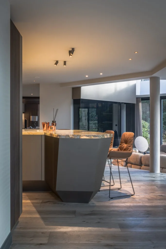 Detail van een geometrisch gevormde bar in de Metropolitan Luxury villa met een verlicht onyx barblad, cognac lederen barkrukken en zicht op de verzonken lounge door ERIC KANT.