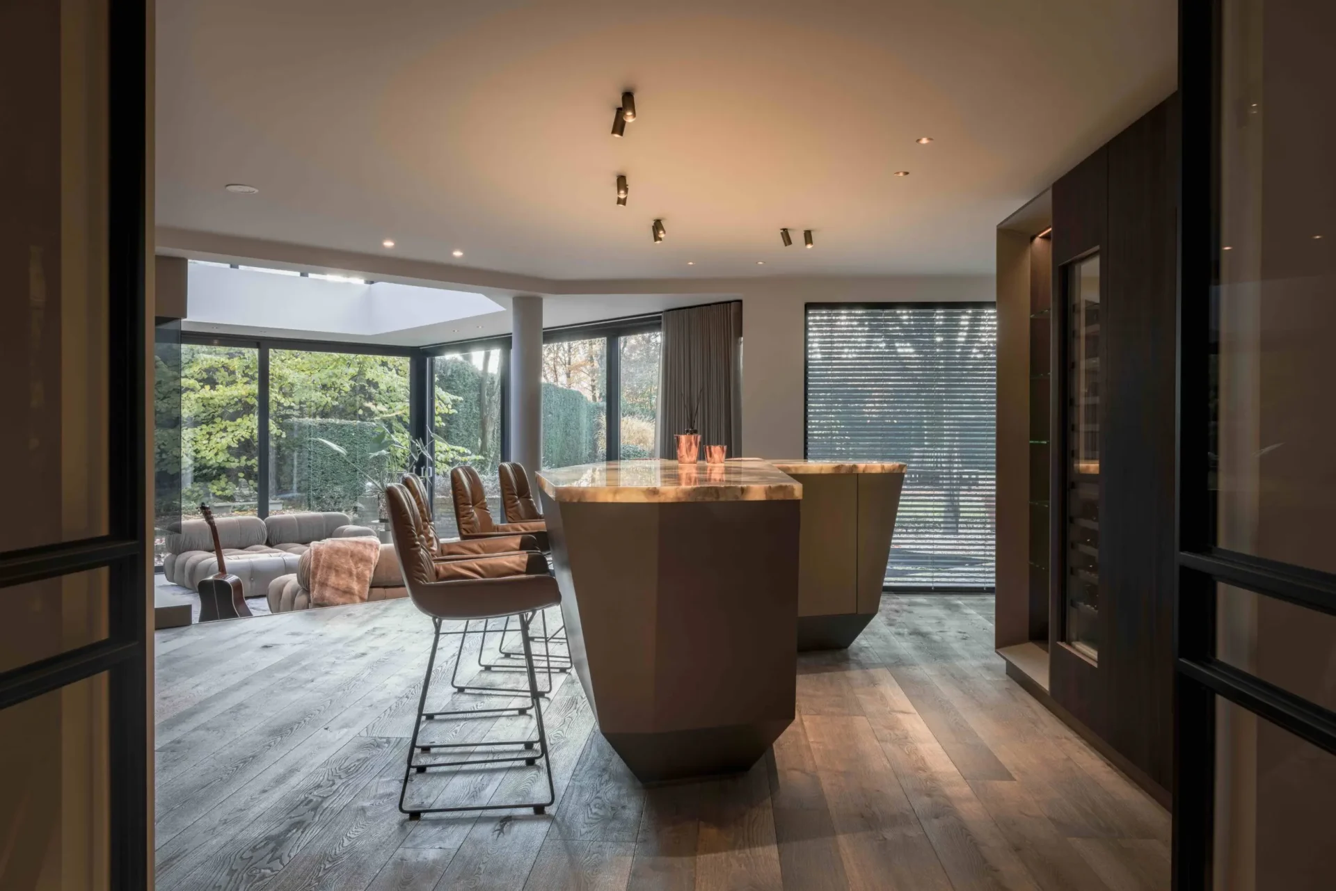 High-end interieur van de Metropolitan Luxury villa door ERIC KANT met een sculpturale bar, zicht op de verzonken lounge en grote raampartijen die uitkijken op de tuin.