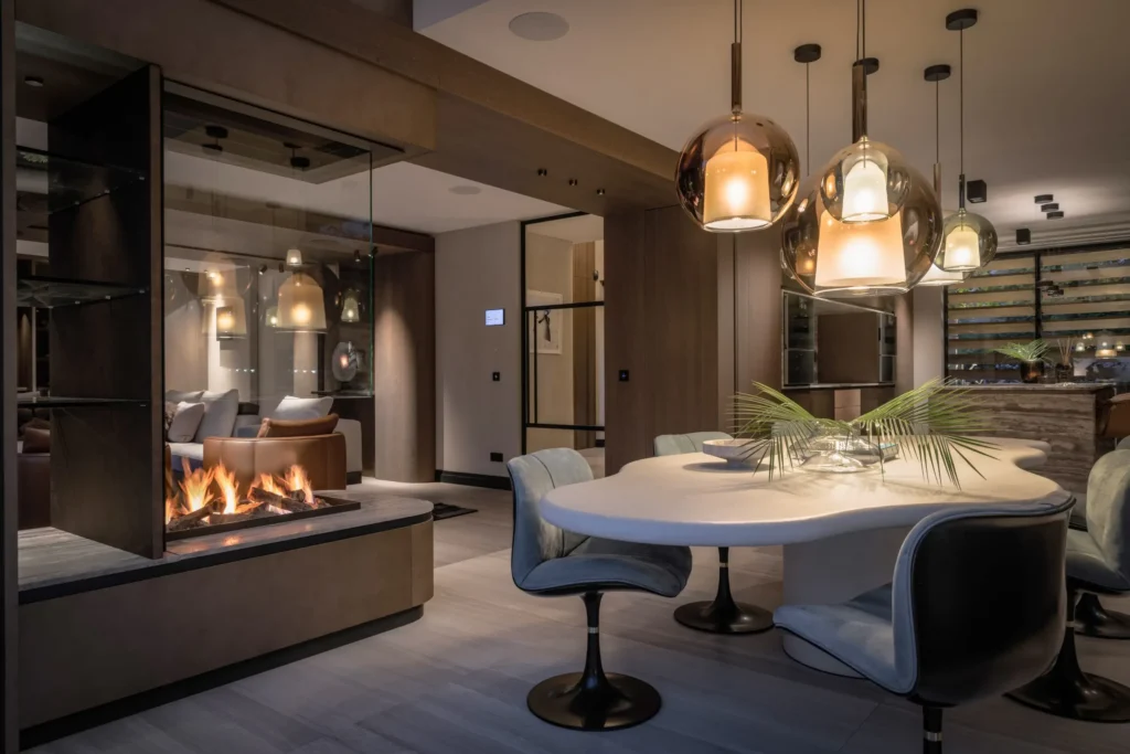 Interieur van een luxe eetkamer in Project 1496 door ERIC KANT met een organisch gevormde eettafel, moderne hanglampen van glas, een doorkijkhaard en fluwelen designstoelen.