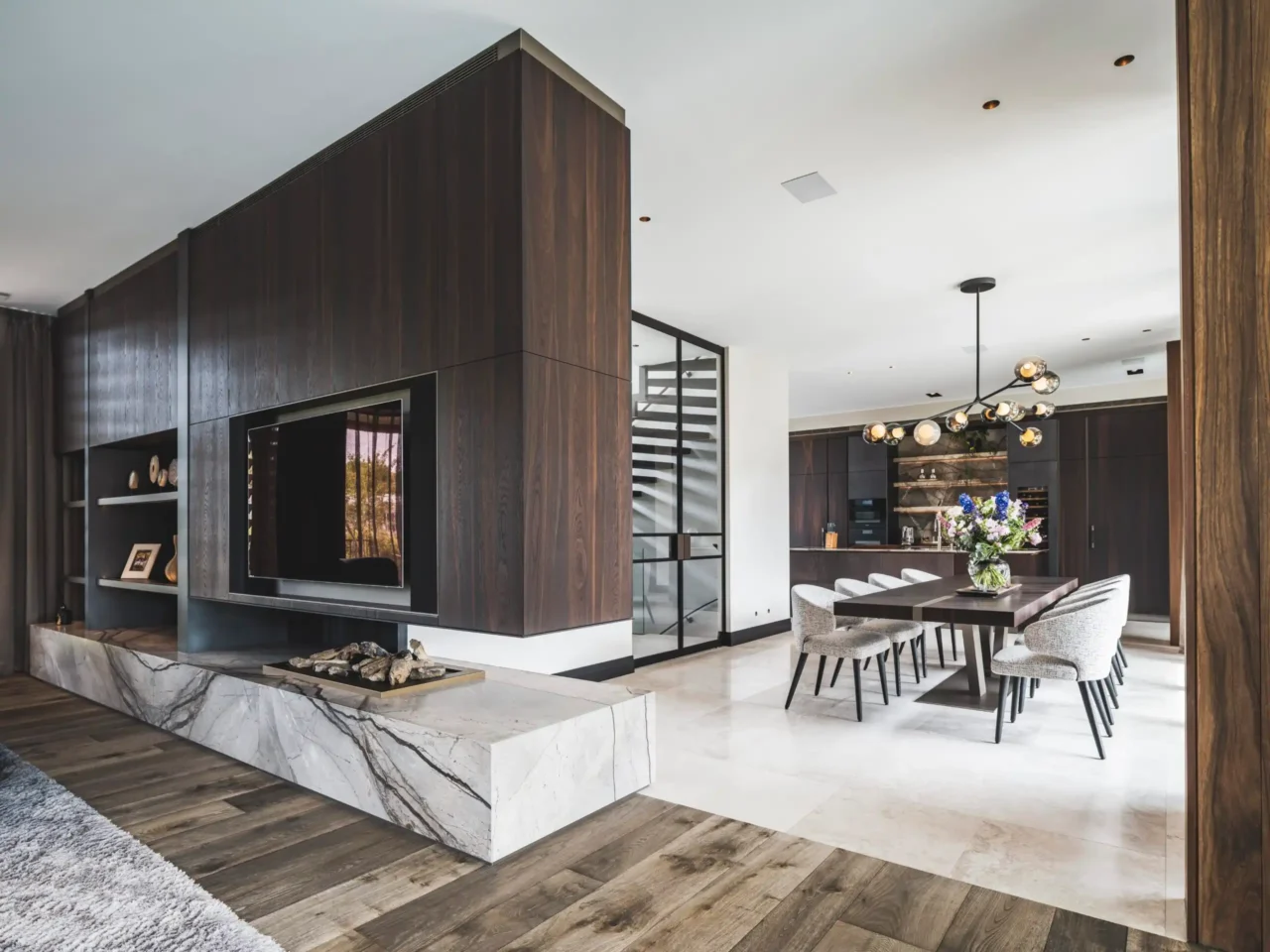 Luxe open interieur ontworpen door Eric Kant, met een maatwerk tv-meubel van donker hout en marmer, een ruime eethoek met Bocci verlichting en een moderne open keuken op de achtergrond.