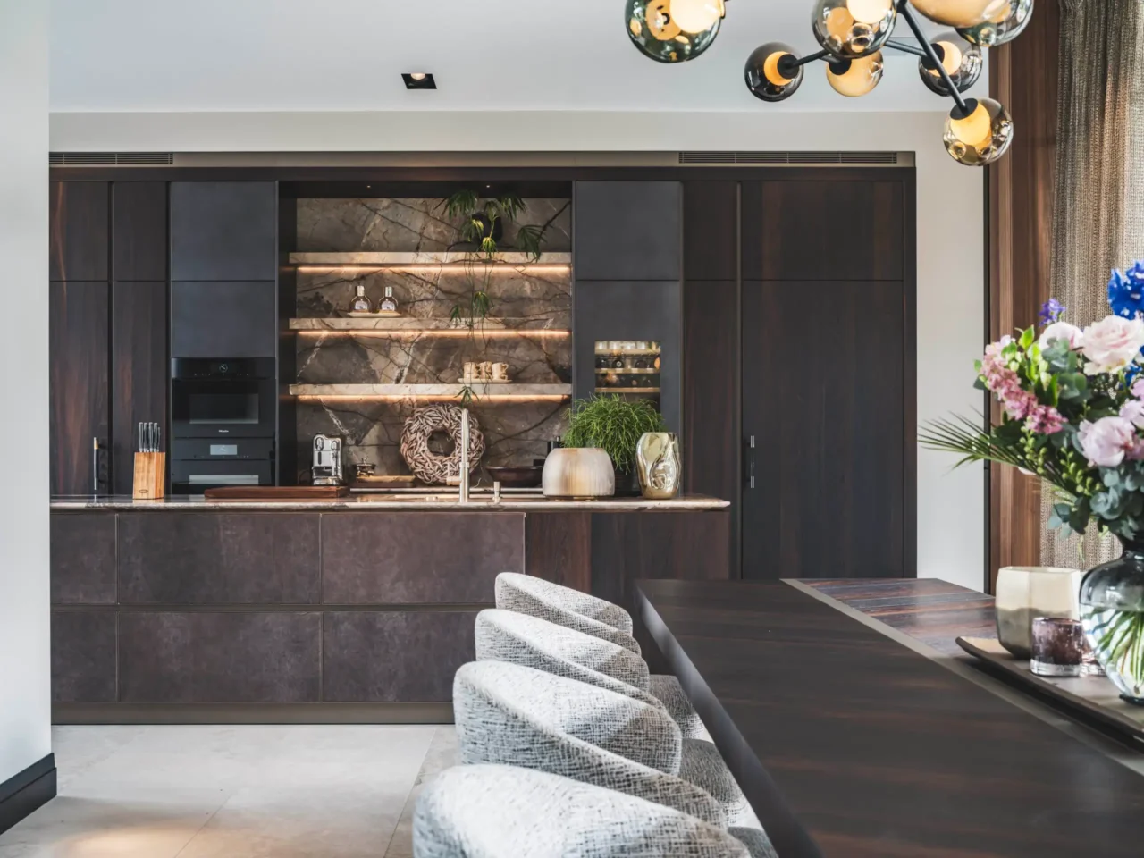 Luxe moderne keuken ontworpen door Eric Kant in samenwerking met Culimaat, voorzien van een kookeiland, donker eiken kastenwanden, verlichte natuurstenen nissen en Miele inbouwapparatuur.