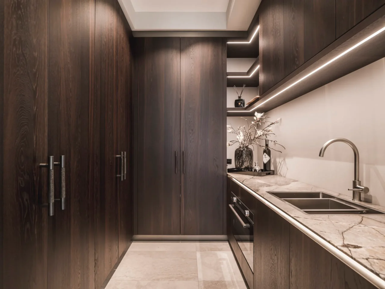 Exclusieve bijkeuken ontworpen door Eric Kant in samenwerking met Culimaat, met donker houten kasten, een natuurstenen werkblad, geïntegreerde oven en sfeervolle led-verlichting.