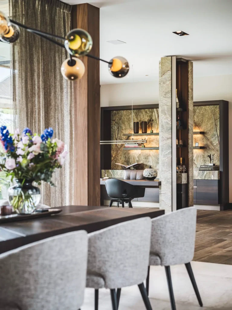 Luxe eetkamer ontworpen door Eric Kant met een kleurrijke Bocci hanglamp, grijze Minotti stoelen en een maatwerk thuiskantoor met verlichte marmeren achterwand op de achtergrond.